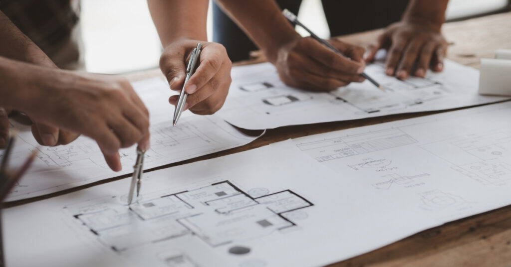 Architects collaborating on building blueprints, reviewing and drawing plans on a desk