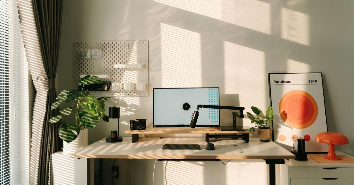 Modern home office setup with minimalist interior wall decor ideas, featuring abstract wall art, indoor plants, and natural light creating soft shadows on a clean white wall.