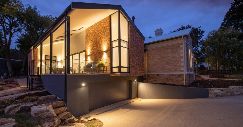 A modern house with large windows and warm lights glowing at dusk.