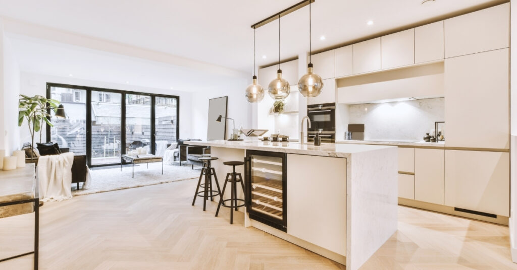 Bright modern kitchen with white cabinets, built-in appliances, island seating, and large glass doors opening to the living area.