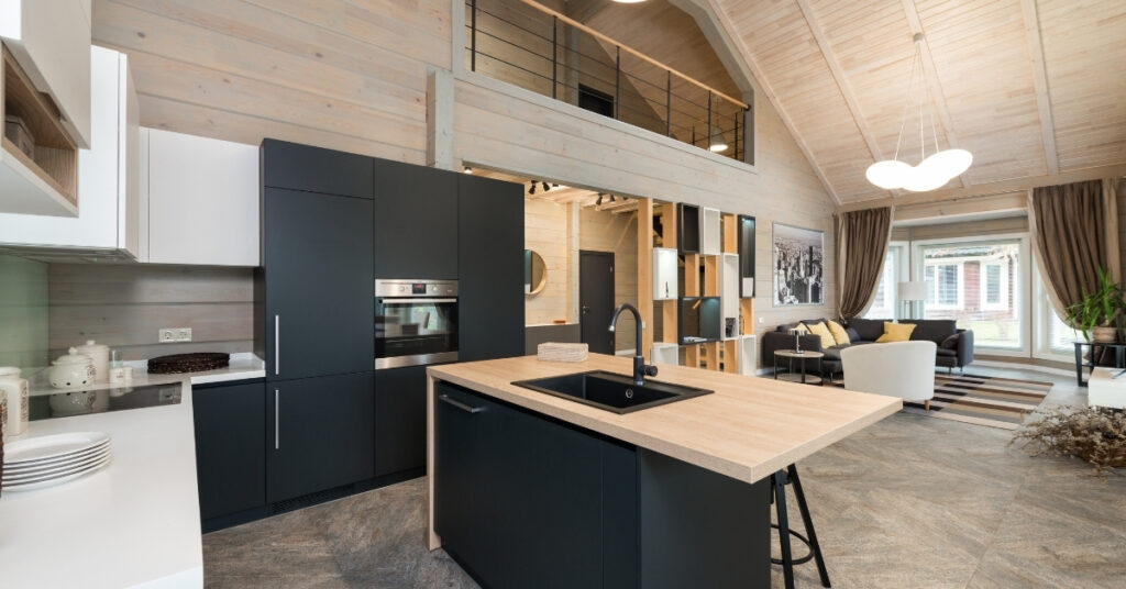 Contemporary open-plan kitchen with black cabinets, wooden island countertop, and modern living area in the background.