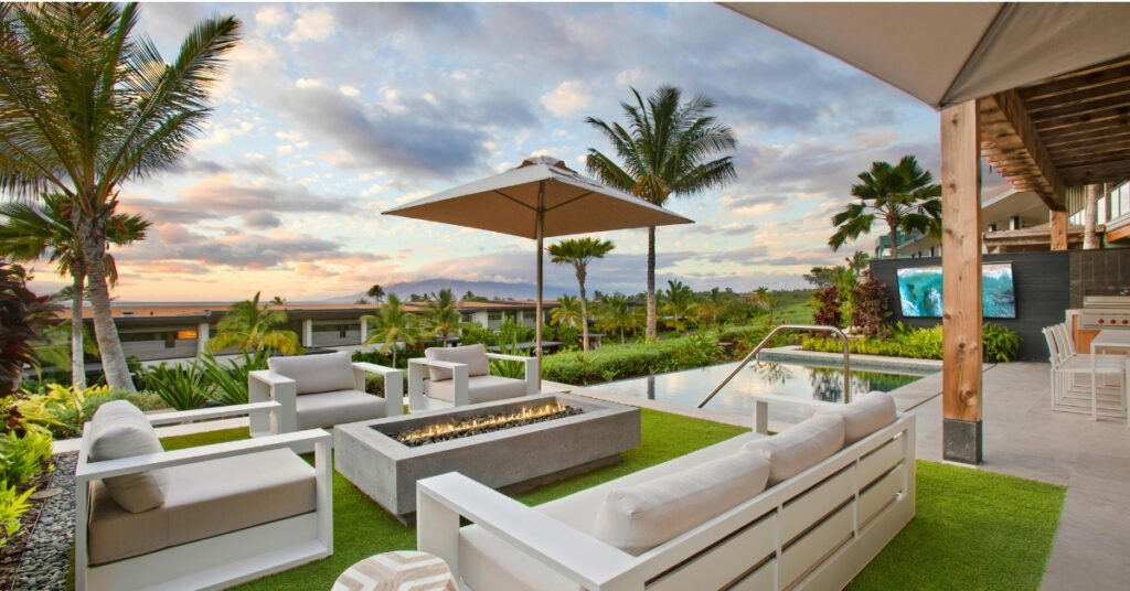 A stylish outdoor space with white furniture, a fire pit, palm trees, and a sunset view.