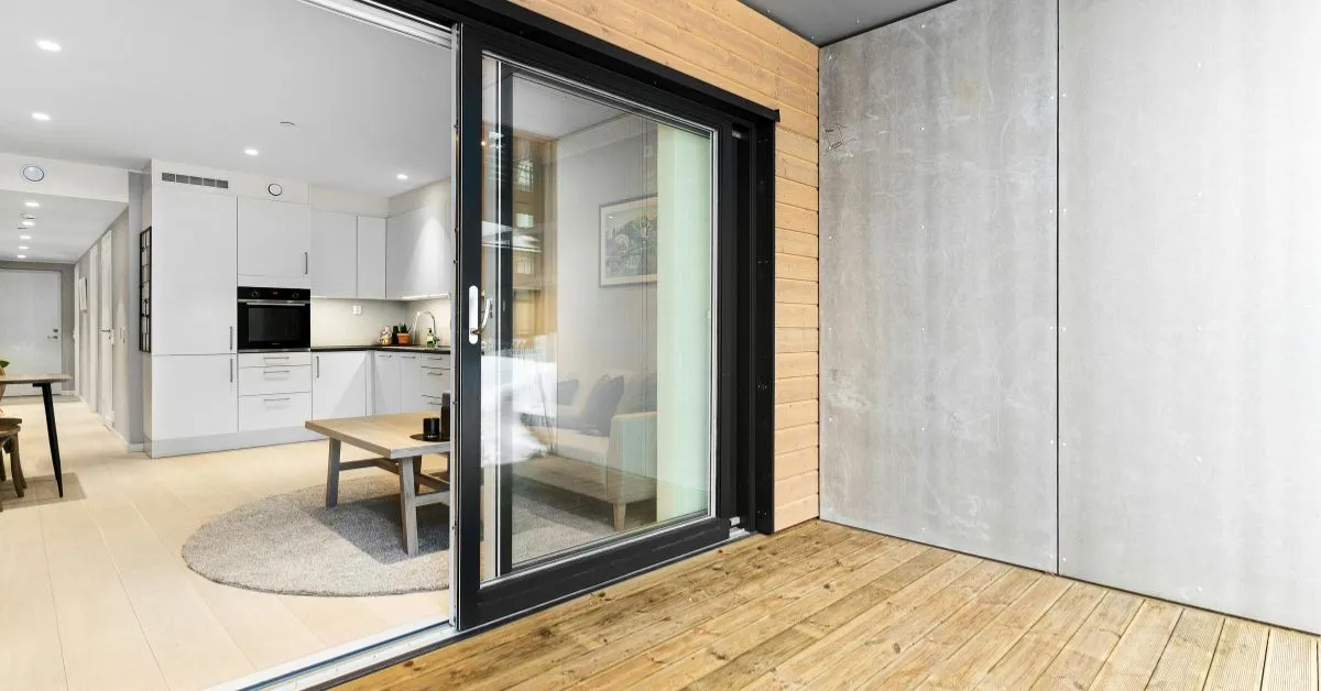 A modern aluminium sliding door leading to a wooden deck, with a glimpse of a contemporary interior design visible through the door, highlighting a clean, minimalist aesthetic.