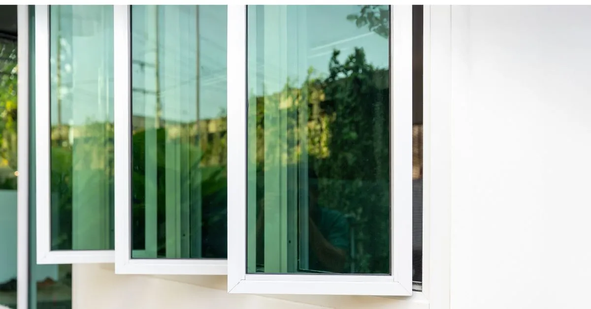 Close-up of a set of modern aluminium windows with sliding panels, offering a clear view of the outdoor greenery through the large glass panes.