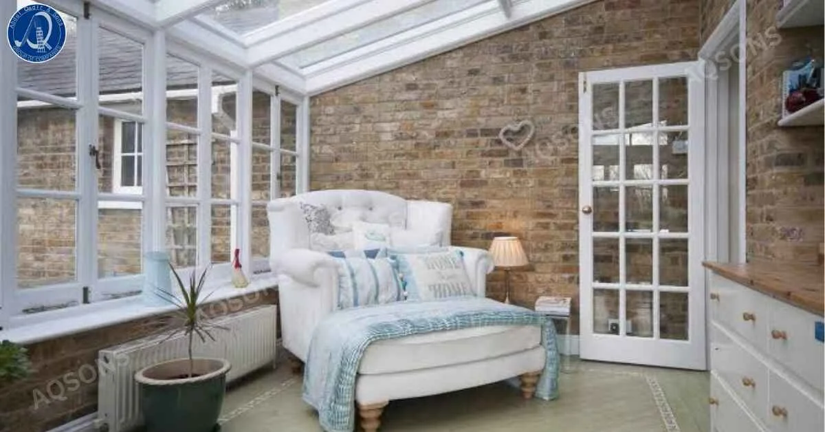 Bright conservatory house extension featuring a glass roof, large white-framed windows, exposed brick walls, and a cozy armchair with soft furnishings, creating a comfortable and light-filled living space.
