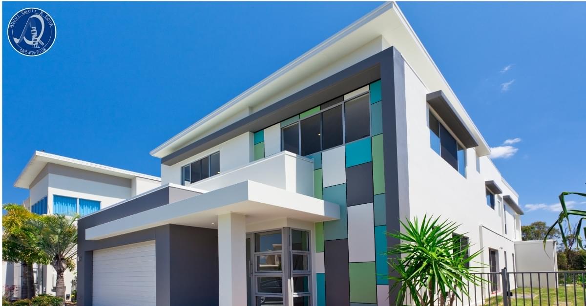 Modern house design with a flat roof, large windows, white and gray exterior, and blue-green accent panels.